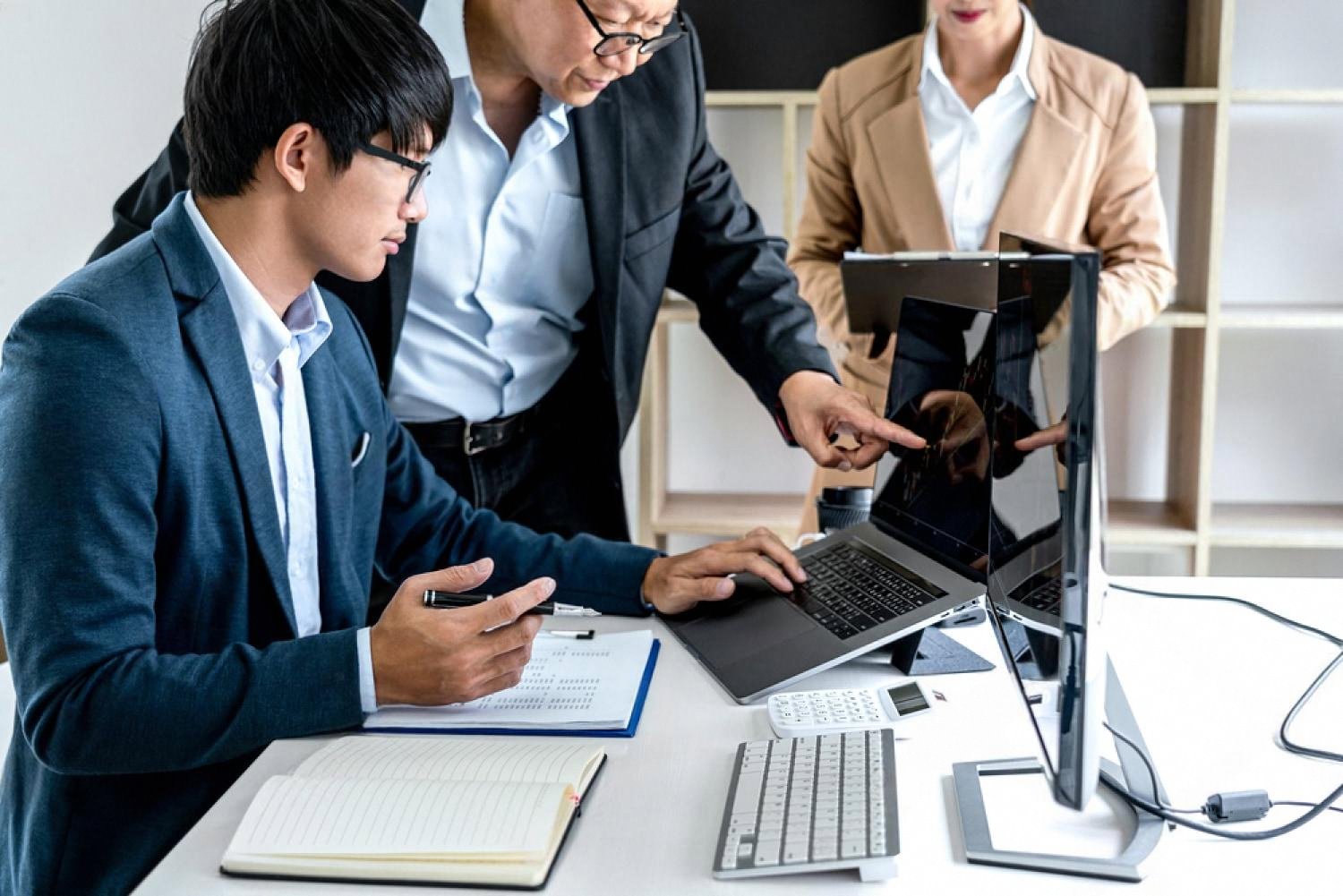 Three business analysts reviewing risk data on a laptop and monitor in a UAE office